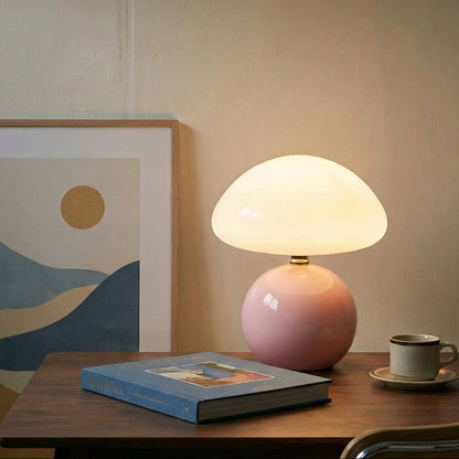 Pink table lamp on a wooden surface with a book and cup in a room setting.
